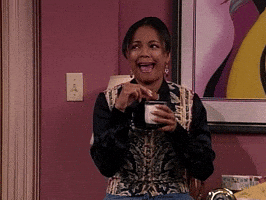 TV gif. Kim Fields as Regine holds a cookie over a mug as she looks to the side and laughs. 