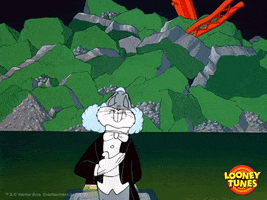 Cartoon gif. Bugs Bunny is standing in front of a giant pile of rubble while wearing a tuxedo and wig. He closes his eyes as he gives us a couple formal bows.