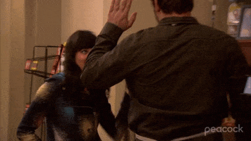 Parks and Recreation gif. Crossing paths, Chris Pratt as Andy and Aubrey Plaza as April give each other high fives and then low-fives.
