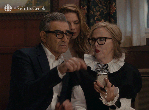 Gif of the cast of Schitt's Creek fighting over a phone while Eugene Levy asks "which way do you swipe to get rid of this one?"