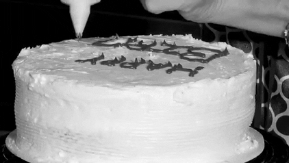 An animated gif. It's a black and white video of a woman icing a birthday cake, that zooms in on the cake to see she ran out of space and so it says "HAPPY BIRTHD"