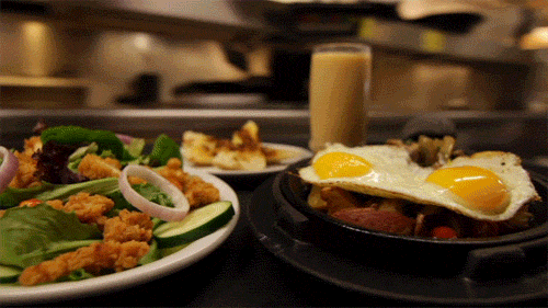Video gif. On a serving tray sits three different plates of food and a large glass of orange juice as the video follows the food from inside the kitchen to the dining area. 