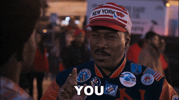 Movie gif. Eddie Murphy as Randy in Coming to America is wearing a New York souvenir baseball cap and multiple souvenir pins on his shirt. He points at the man in front of him and says, “You.”