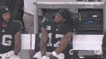 Sports gif. Davante Adams of the Las Vegas Raiders is sitting on the sidelines looking cool as he vibes and nods his head in slow motion, long dreads flying all over the place and hitting him in the face.