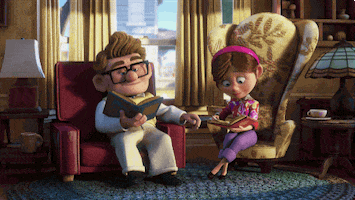 Disney gif. Carl and Ellie Fredrickson from Up are adults and sit in their living room. They both read books in separate chairs while they hold hands. 