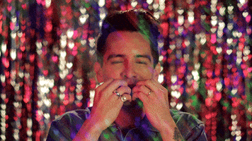 Celebrity gif. Brendon Urie from Panic at the Disco among a glittery, shiny, confetti-filled environment, with his eyes closed, kisses his fingers and raises his arms with elation.
