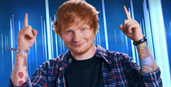 Celebrity gif. Ed Sheeran looks at us with a smile, pointing up above his head with both arms.