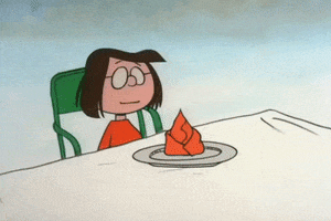 TV gif. Peppermint Patty in A Charlie Brown Thanksgiving sits at a table with a napkin folded nicely in front of her. To her surprise, a plate full of food flies toward her, knocking the fancy place setting away.