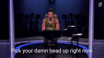 Video gif. Chipper Peloton instructor rides a Peloton and says to us, “Smile. You woke up. Pick up your damn head right now.”