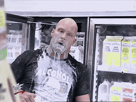 TV gif. Stone Cold Steve Austin, his mouth and body dripping with milk, stands in the doorway of a convenience store fridge door and raises up a half-gallon of milk to cheers, nodding.