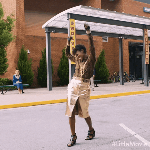 Movie gif. Issa Rae as April in Little pumps her arms triumphantly, walking away from a brick building.