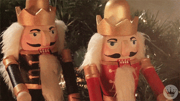 Stop motion gif. Two nutcrackers, one in red and the other in blue, drop their jaws and arms as if shocked at something, one after the other, chunks of walnut falling out of the mouth of the 2nd.