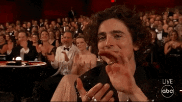 Celebrity gif. Timothée Chalamet sits in the audience at the 2022 Oscars, smiling and clapping. 
