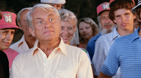 Movie gif. Ted Knight as Judge Smails in Caddyshack stands in a crowd and screams at someone offscreen, punctuating every syllable with a lot of sass. Text, Well, We're Waiting.