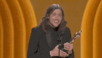 Oscars 2024 gif. Ludwig Göransso wins best original score for Oppenheimer. He shakes the Oscars trophy by its base and stares at someone in the crowd while saying, "Thank you for getting me guitars and drum machines instead of video games."