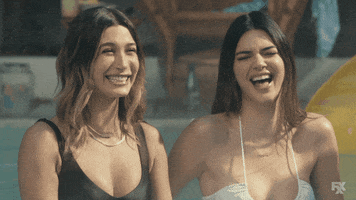 TV gif. Kendall Jenner and Hailey Bieber as themselves, falling into each other in mocking, mean-girl laughter.