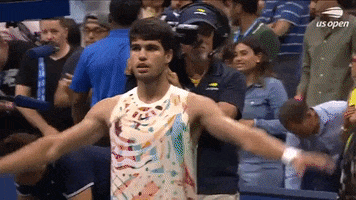 Sports gif. Carlos Alcaraz of Spain walks on the court at the 2023 US Open, wearing a colorful graphic t-shirt. He raises his arms out and then flips his palms to look up at the sky or fans in the stands like he's going for glory.