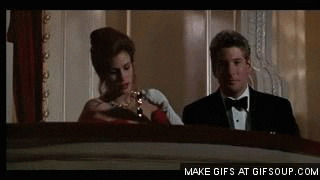 Movie gif. Julia Roberts as Vivian in Pretty Woman fumbles with opera glasses before Richard Gere as Edward adjusts them for her in a balcony at a theater.