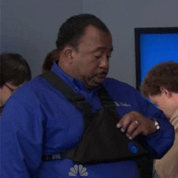 The Office gif. Leslie David Baker as Stanley stands boredly in a room full of people. He has a triangular pouch strapped to his chest. He unzips it and unapologetically takes out a slice of pizza out of the pouch. He then goes in for a big bite.