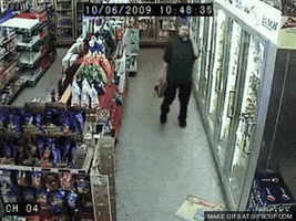 Video gif. Surveillance footage inside a convenience store shows a man carrying a six-pack walking and then falling over sloppily onto his back, apparently drunk.