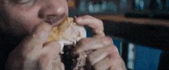 Movie gif. Tom Hardy as Eddie Brock in Venom tears into a rotisserie chicken leg. His eyes change from regular pupils to all white and then to all black as Venom takes control. 