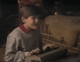 Video gif. Young boy has an old chunky keyboard on his lap and he throws a fist in the air in celebration as he says, “Alright!”