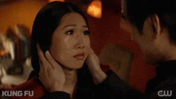 TV gif. Shannon Dang as Althea on Kung Fu smiles slightly, heartened, at Tony Chung as Dennis, who cradles her face with his hands and then embraces her.