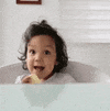 Video gif. A toddler sits at a table with a cracker in her hands. She looks at us with a big excited smile and then grins while giving a big thumbs up. Text, “Thank you!”