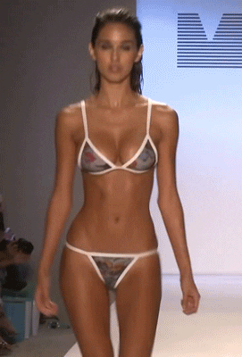 Celebrity gif. Ashley Sky walks the runway modeling a bikini, boobs jiggling. 