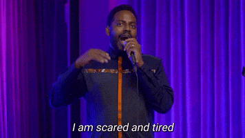 TV gif. Baron Vaughn on The Joka, doing stand-up on-stage, gesturing with his hand and smiling as he says, "I am scared and tired all of the time, just, terrified and exhausting. I don't know about you, but every morning I wake up like, 'Is the world ending or am I still paying rent?'"