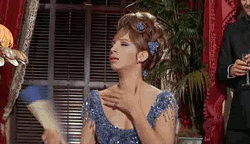 Movie gif. Barbra Streisand as Fanny in Funny Girl. She's wearing an evening ball gown and she fans herself dramatically with a huge fan while clutching her chest.