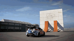 Video gif. Flashy car with a blue, white, and orange design drives up an orange ramp leaning against a white wall. It swerves and spins along the wall before barreling down backwards on the other orange ramp.