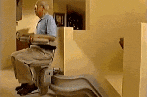 Video gig. An old man sits in a stair lift that goes down his stairs. At the end of the steps is a pool of lava. The man looks down in fear as he reaches closer and closer to the hot flames.