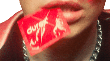 Music video gif. Close-up of Yungblud's mouth, clenching the corner of a red Durex condom with his teeth.