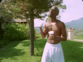 Music video gif. Close up of 2Pac fanning himself with his hand in a backyard in the music video, "I Get Around."