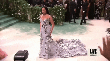 Met Gala 2024 gif. Demi Lovato poses for the cameras stiffly turning side to side wearing a smokey lavender Pabral Gurung gown embellished with silver flowers.