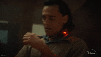 TV gif. Tom Hiddleston as Loki in Loki. He's in jail and has a collar around his neck to prevent him from using his powers. He's sitting in a chair and frustratedly drops his head into his hands.