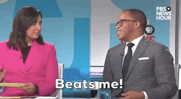 TV gif. Jonathan Capehart and Amna Nawaz seated behind the news desk on PBS Newshour. Nawaz shakes her head in response to Capehart who tosses a hand away, saying "Beats me!" which appears as text.