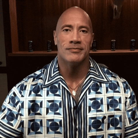 Celebrity gif. Dwayne Johnson raises his hand to give a salute and smiles.