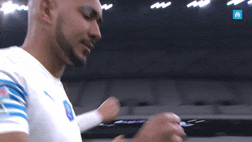 Sports gif. Dimitri Payet walks on the soccer pitch clapping his hands.