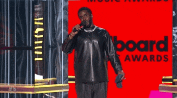 Celebrity gif. P Diddy shakes his head and smiles while spreading his arms out to the side, as if to express "whatever," on stage at the Billboard Music Awards.