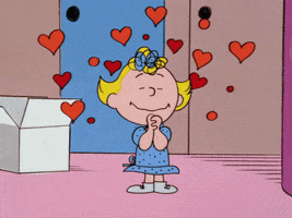 Cartoon gif. Sally from the Peanuts gang closes her eyes with her hands clasped together as she smiles and heart shapes dance around her head. 