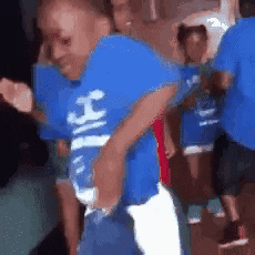 Video gif. A close-up of a Black child doing the Milly Rock dance among a group of other kids.