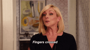 TV gif. Jane Krakowski as Jacqueline White on The Unbreakable Kimmy Schmidt has a positive smile on her face as she holds up crossed fingers on both hands. She says, “Fingers crossed.”