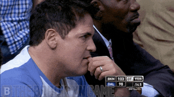 Sports gif. Wearing a blue and white baseball t-shirt, an angry Mark Cuban seems to be swearing out loud while watching a basketball game. 