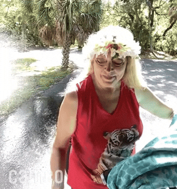 Celebrity gif. Closeup of Carol Baskin reaching forward then stumbling back as she's blasted with a spray of water.