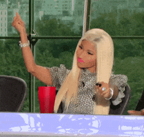 Celebrity gif. Nicki Minaj on American Idol, dancing in her seat. She looks hype, dancing with her arms up and does a chest pulse dance move. 