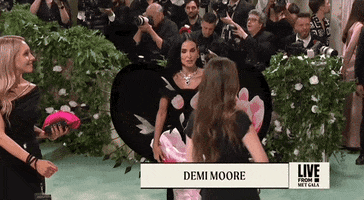 Met Gala 2024 gif. Demi Moore takes quick mini steps forward towards the camera showing the stiff structure of the large petals edged with black thorns. The form fitting column dress has exaggerated hip detailing to create a scalloped silhouette.
