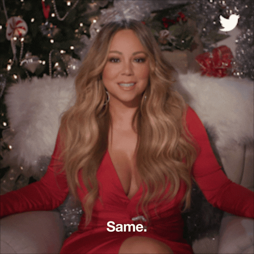 Celebrity gif. Mariah Carey wears a festive red dress with Christmas decorations displayed behind her as she gently shakes her head as if in agreement. Text, "Same."