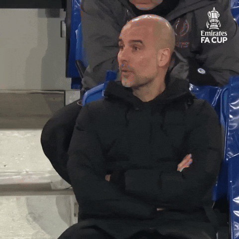 Sports gif. Pep Guardiola, manager of Manchester City, is watching a soccer game, very upset by the outcome of the play. He drops his hands into his lap before crossing his legs and covering his face with his hand in defeat.